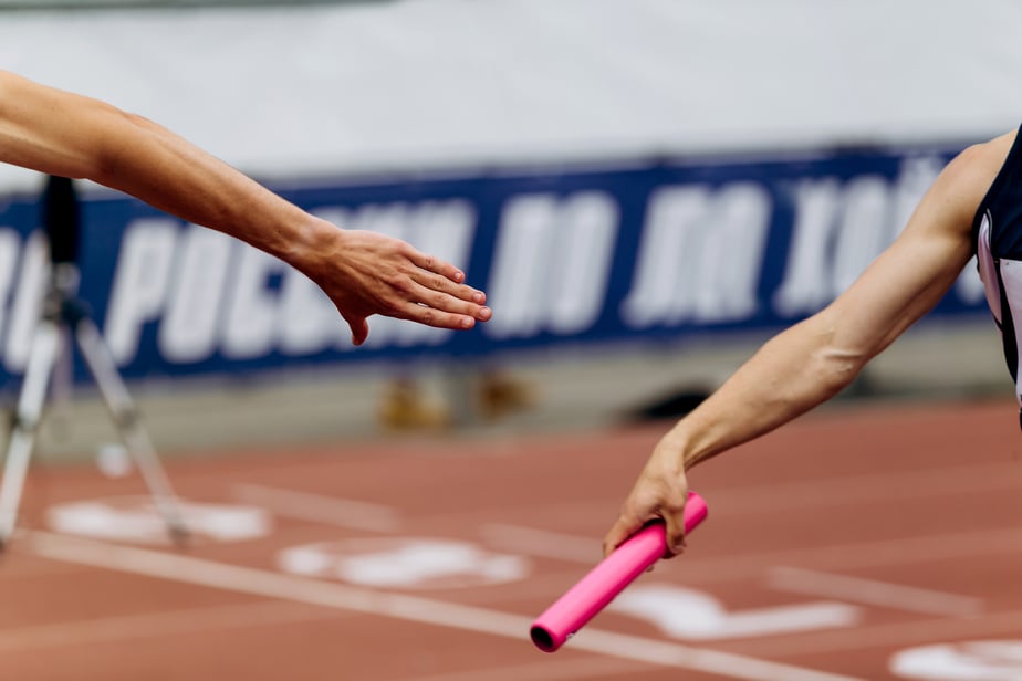 Teammate passing baton during a race to show teamwork