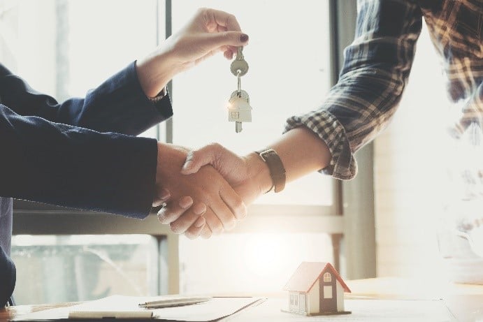 Close up of a real estate agent holding the keys to a new home and shaking the hand of a buyer