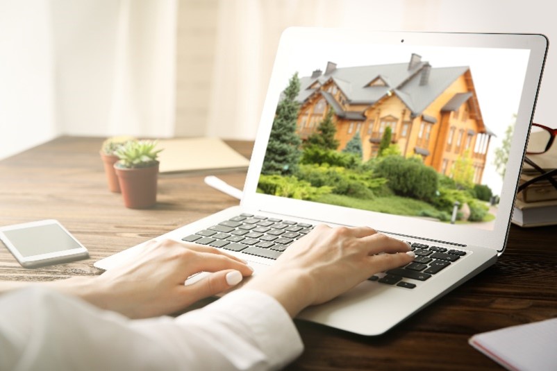 A picture of women’s hands on a laptop keyboard with a full-screen image of a large home on the screen. 